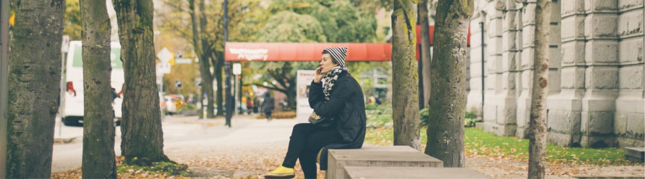 a person in a beanie sits on a bench outside while talking on the phone