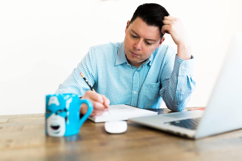 a man with a Captain America mug writes in his notebook