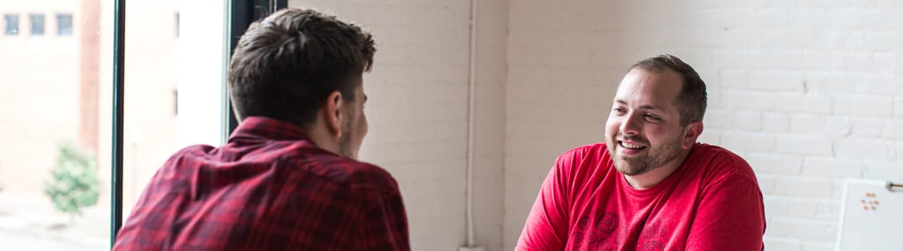 layout by flywheel sell clients on new content management platform from business catalyst two men talking near bright window and white brick wall