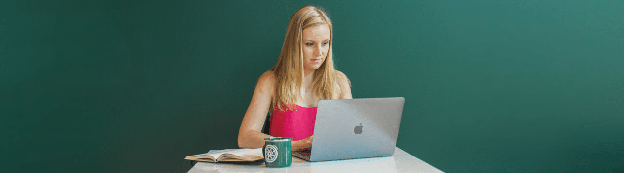 woman writing content marketing ideas in notebook with laptop and flywheel mug nearby