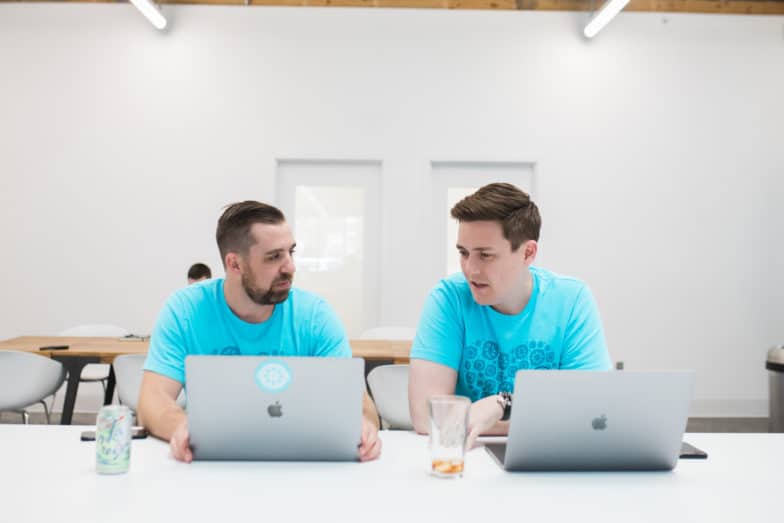 two men in blue shirts collaborate over their laptops in a white room