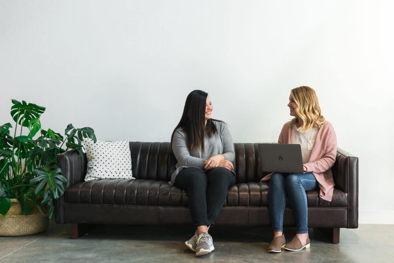 Two women sit on a couch looking at a computer
