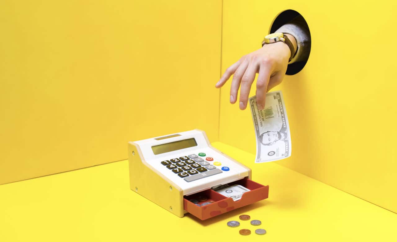 a hand takes a five dollar bill out of a toy cash register