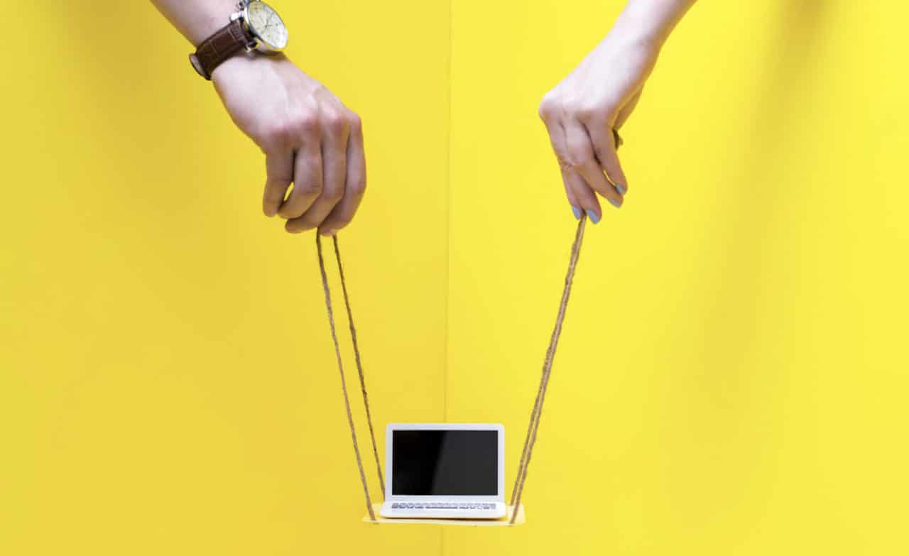 a puppeteer's hands with strings holding up a laptop