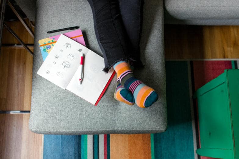 Person's feet and legs next to an open sketchbook.