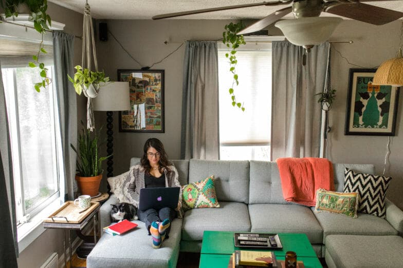 Woman sits on her couch working on a computer. 