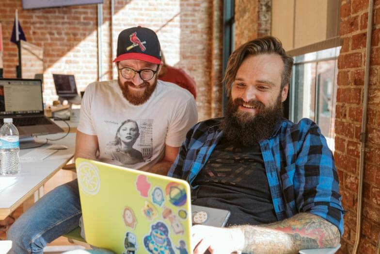 two men smile at their design on a yellow laptop