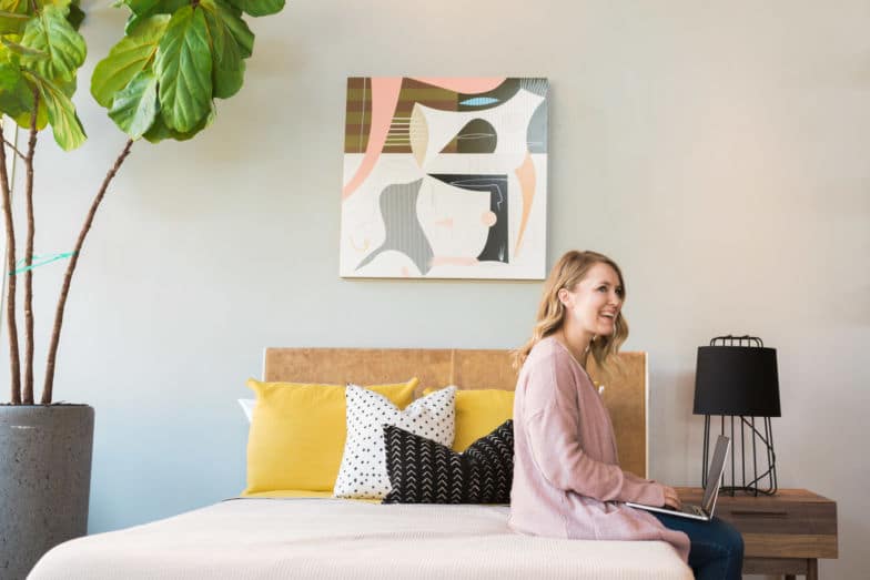 Woman sits on bed working on a laptop