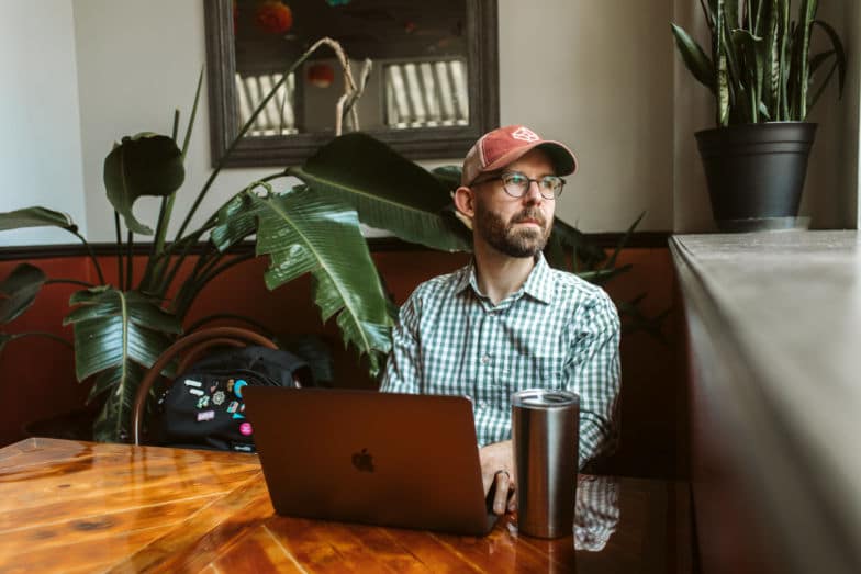 Man works on a computer at a cafe in front of plants 