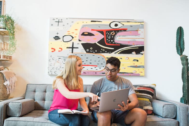 Two people sit on a couch looking at a computer 