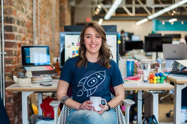 a creative sits at her desk wearing a shirt bearing a rocket