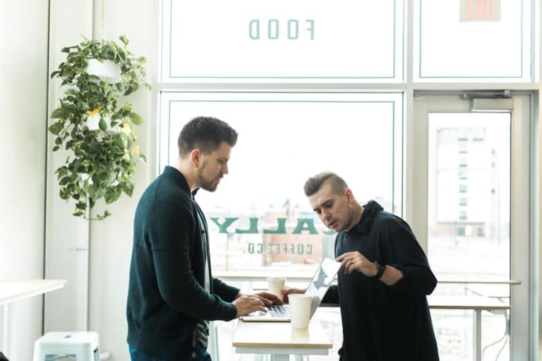Two men look at a computer in a coffee shop.
