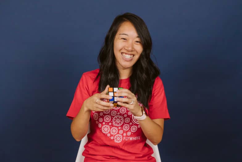 a woman in a red shirt smiles as she solves a rubik's cube