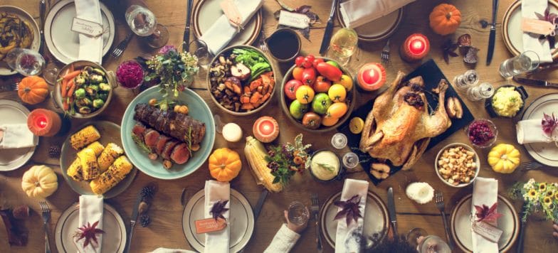 a full Thanksgiving table, including meats, vegetables, candles, and place settings