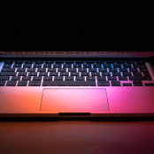 partially closed laptop with screen light illuminating the keyboard in a dark room
