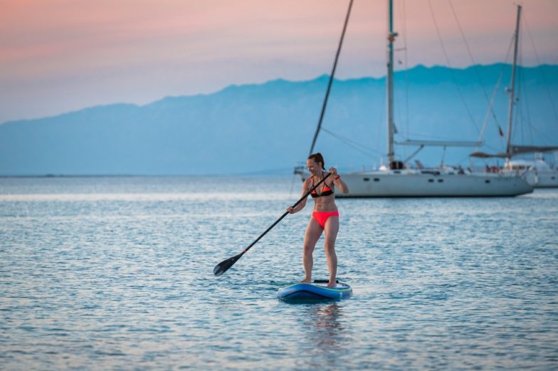 Stock image of a woman paddle boarding on Glacier Lake blue waters in front of a Gossamer Pink sky