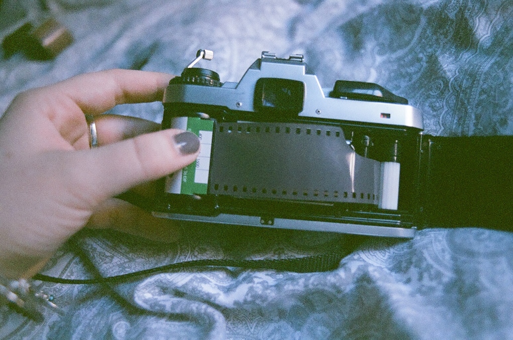 hand with gray painted nails holds a camera, putting a roll of film into place