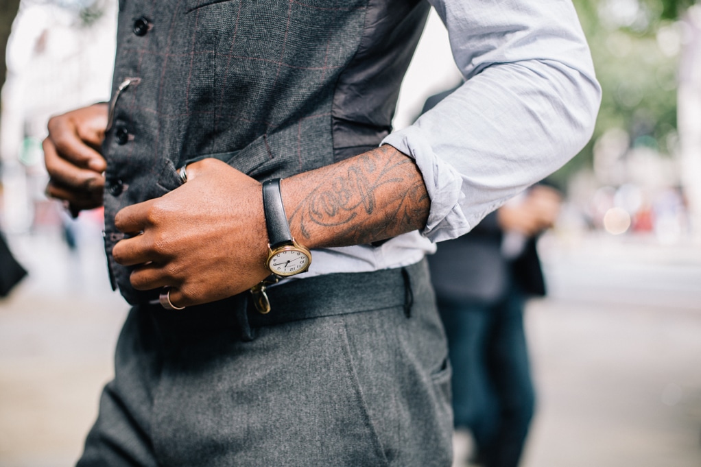 photo depicts the torso of a man wearing a suit vest and a watch with his thumbs hooked into his vest pockets