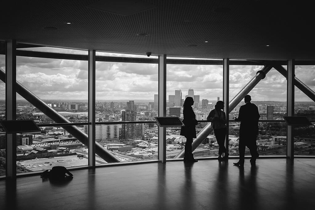 black and white photo of three people talking in front of a window overlooking a city skyline