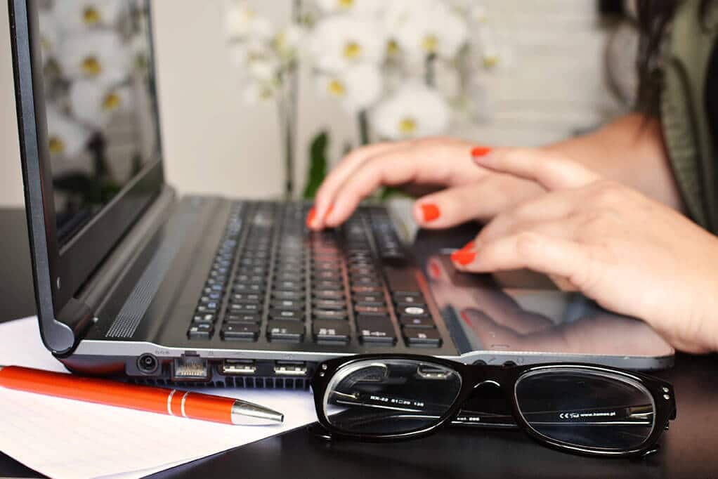 a person with red painted nails types on a computer