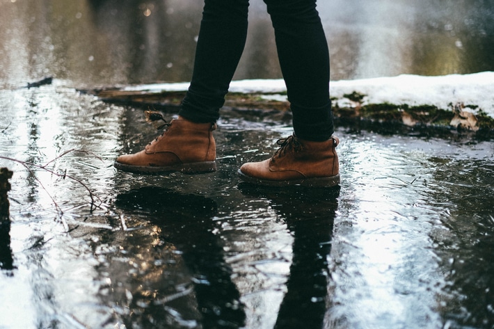 a person wearing brown boots walks outside on wet pavement