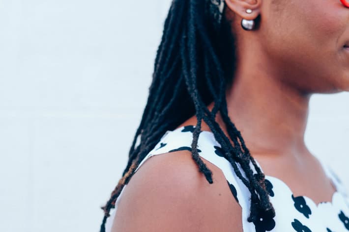 a picture of a woman's profile. She has shoulder-length black hair styled in locs and wears a black and white tank top