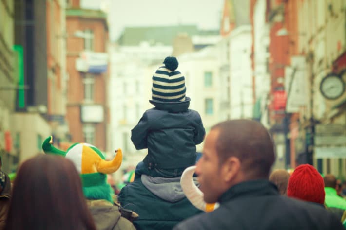 a man carries his child on hit shoulders. they face away from the camera, and the child is wearing a winter hat