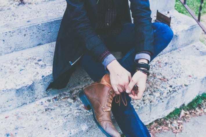 man sits on a concrete step wearing brown leather shoes, dark wash jeans, and a nice suit jacket
