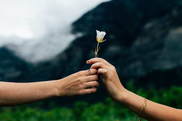 one arm outstretched from the left side of the frame, handing a small white flower to another hand which reached in from the right side of the frame