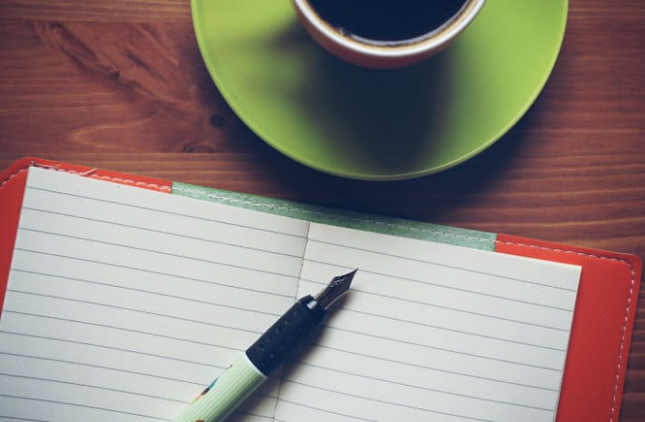 empty lined notebook with a pen next to a coffee mug on a green place