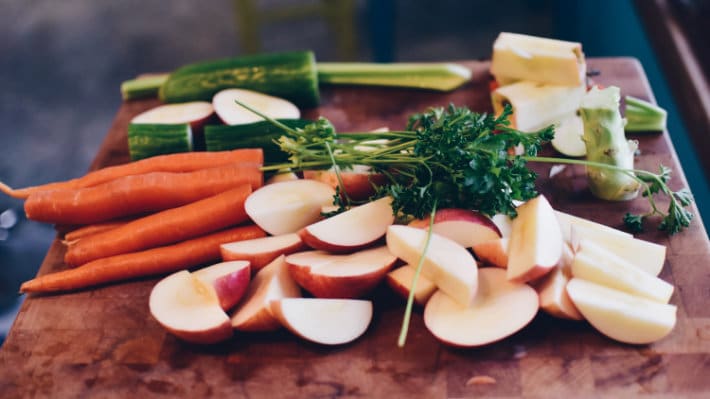 a cutting board with carrots, cucumbers, apples, and fresh herbs