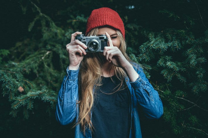 a woman in a red beanie looks through the viewfinder of a camera