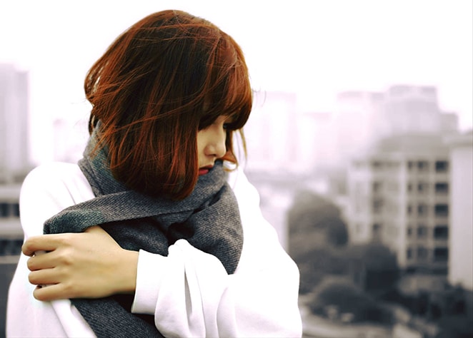 a woman in a white sweater pulls her scarf over her neck to guard against the cold