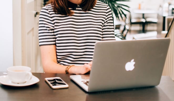 woman in a striped shirt types on a Macbook