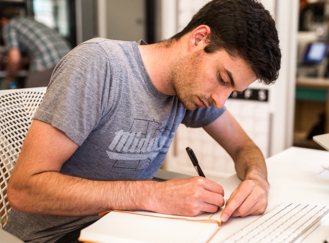 layout by flywheel designer's block man in grey shirt writing in orange journal