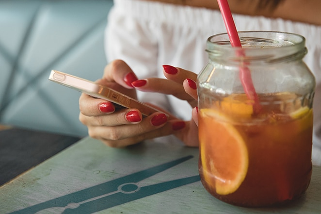 woman with red nail polish and tea with fruit in jar on mobile phone