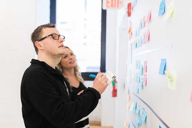 Man and woman plan for user clarity in front of a wall full of multicolored post-it notes