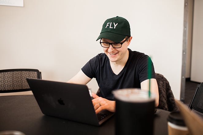 layout by flywheel develop marketing strategy for design agency how to man with simple shirt and table with laptop and baseball hat