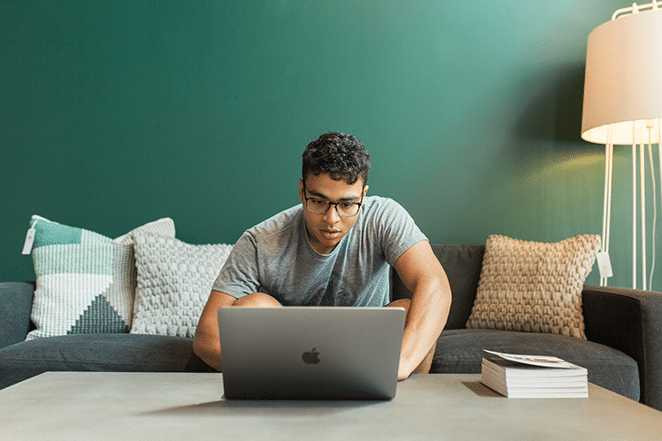 layout by flywheel why wordpress is the best cms in 2018 man leaning over to computer on coffee tbale with stack of books and lamp near grey couch