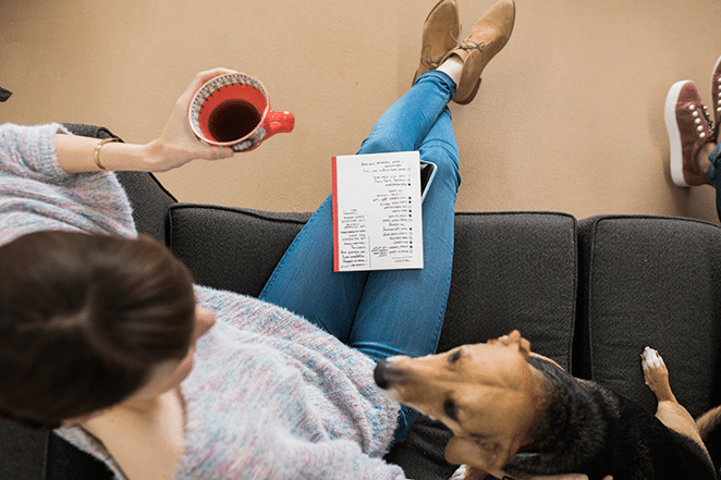 woman and dog on couch with tea in hand and notebook with checklist of content metrics for success